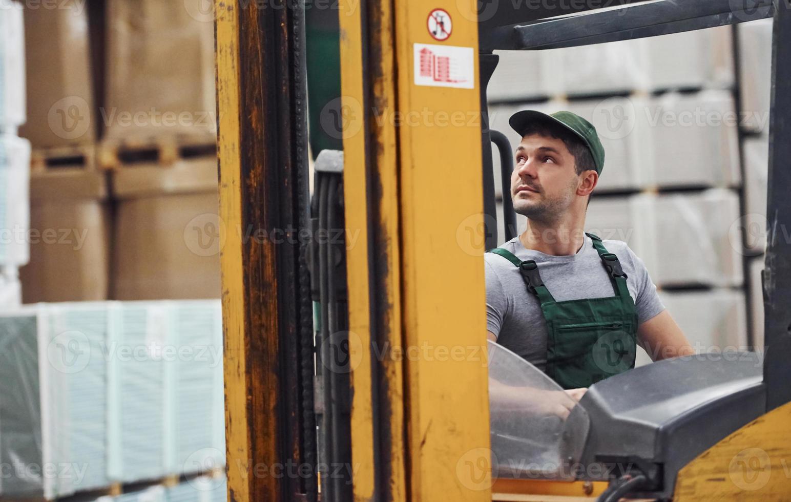 Young worker in unifrom sits in the forklift in the warehouse photo