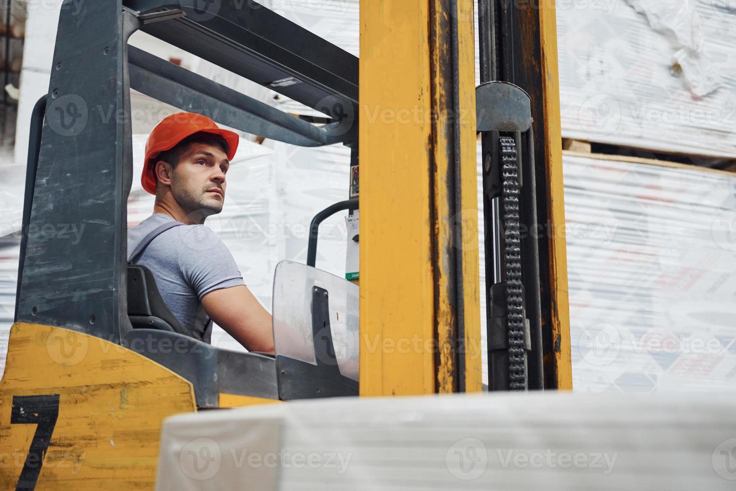 Young worker in unifrom sits in the forklift in the warehouse photo