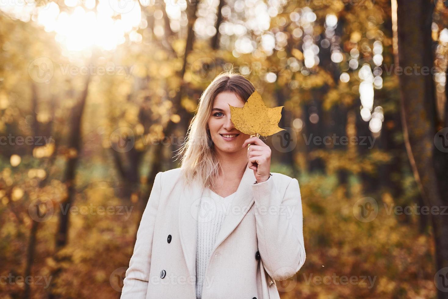 Portrait of young brunette with leaf that is in autumn forest at daytime photo