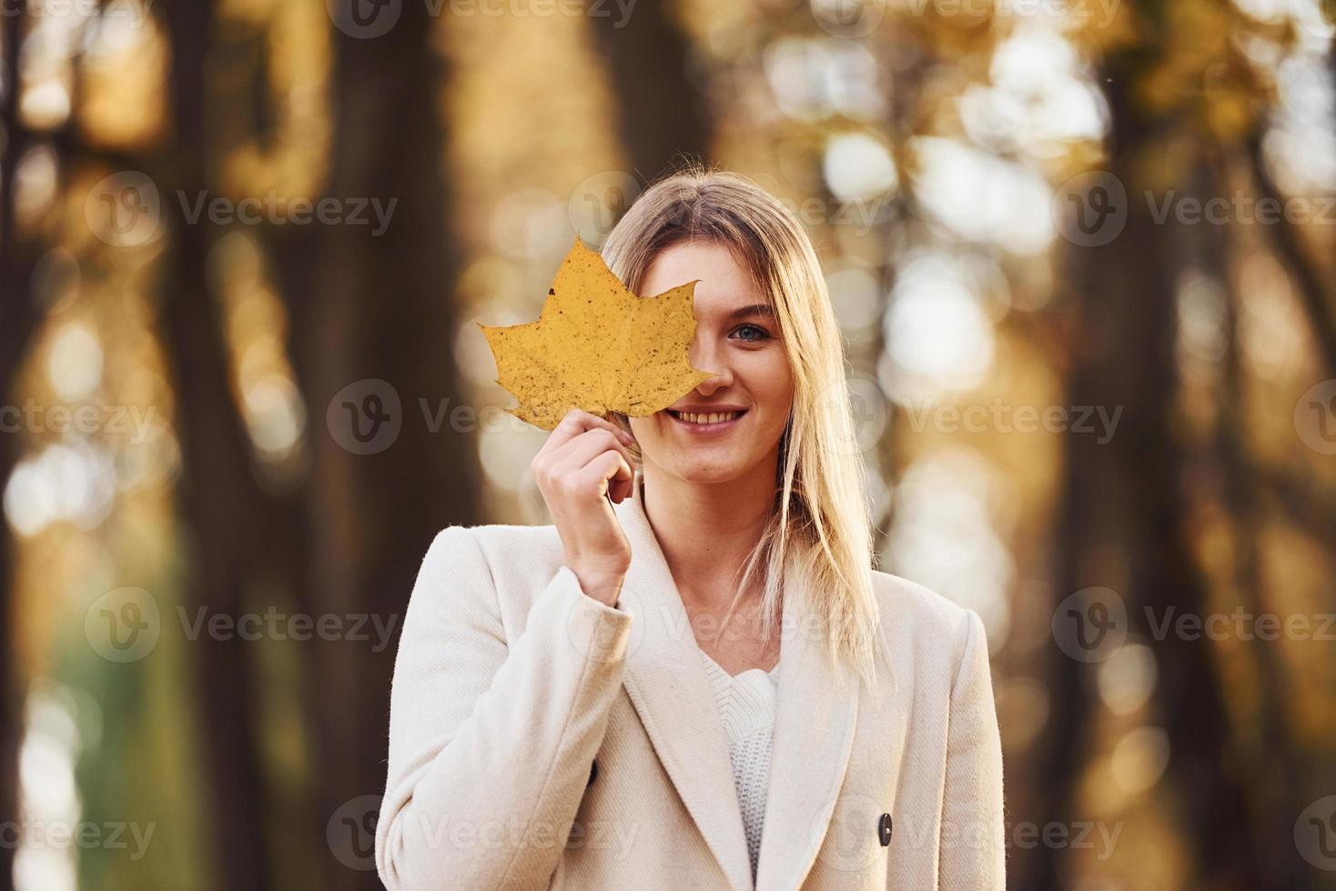 Portrait of young brunette with leaf that is in autumn forest at daytime photo