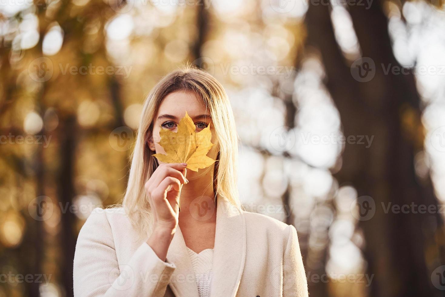 Portrait of young brunette with leaf that is in autumn forest at daytime photo