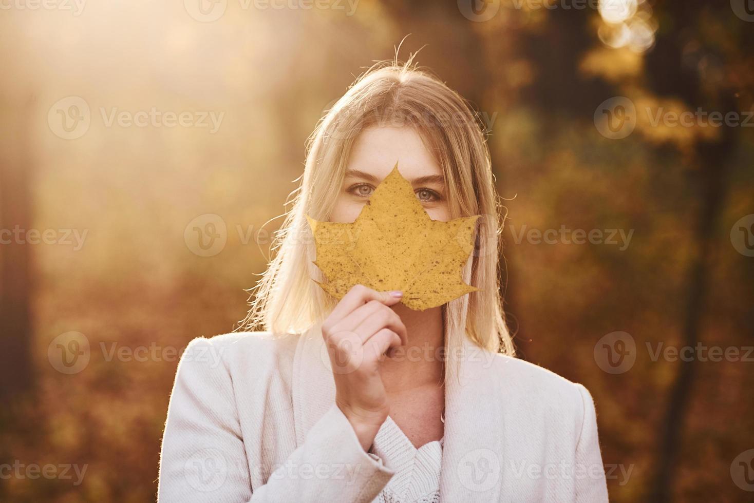 Portrait of young brunette with leaf that is in autumn forest at daytime photo