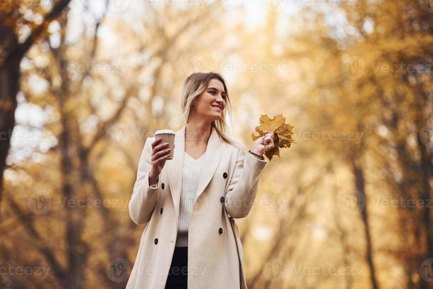 Holds cup of drink. Portrait of young brunette that is in autumn forest at daytime photo