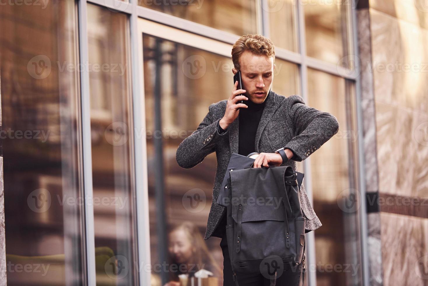 Man in elegant formal wear outside against modern building talking by the phone photo