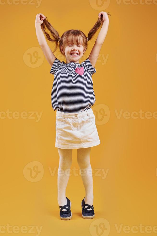 Cute little girl in casual clothes have fun in the studio against yellow background photo