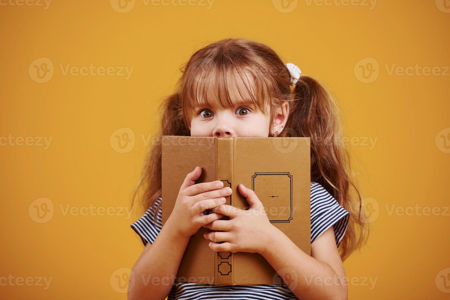 Cute little girl with book in hands in the studio against yellow background photo