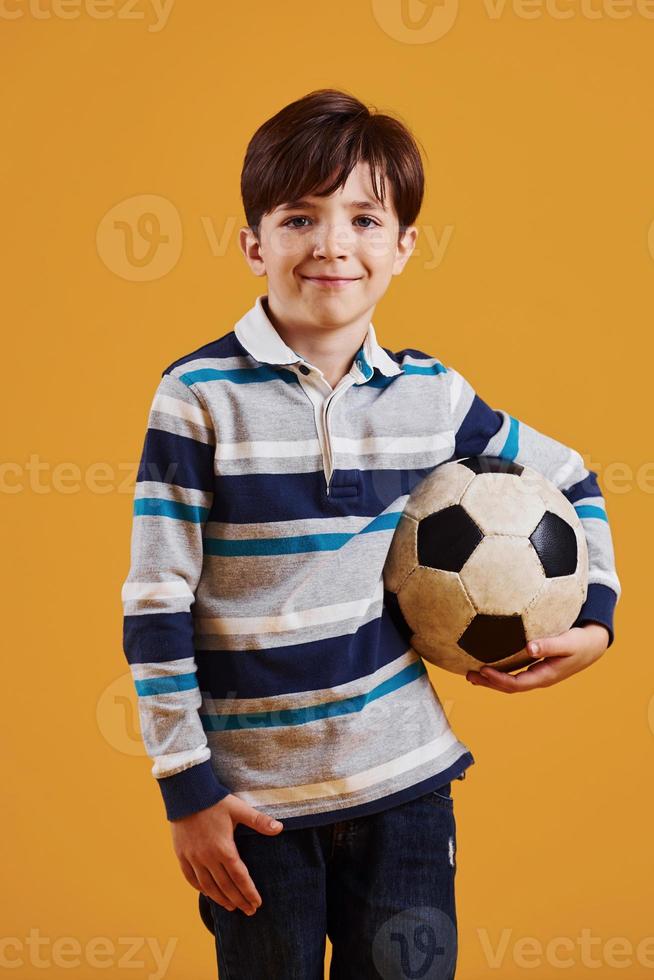 Portrait of young soccer player with ball. Stands against yellow background photo