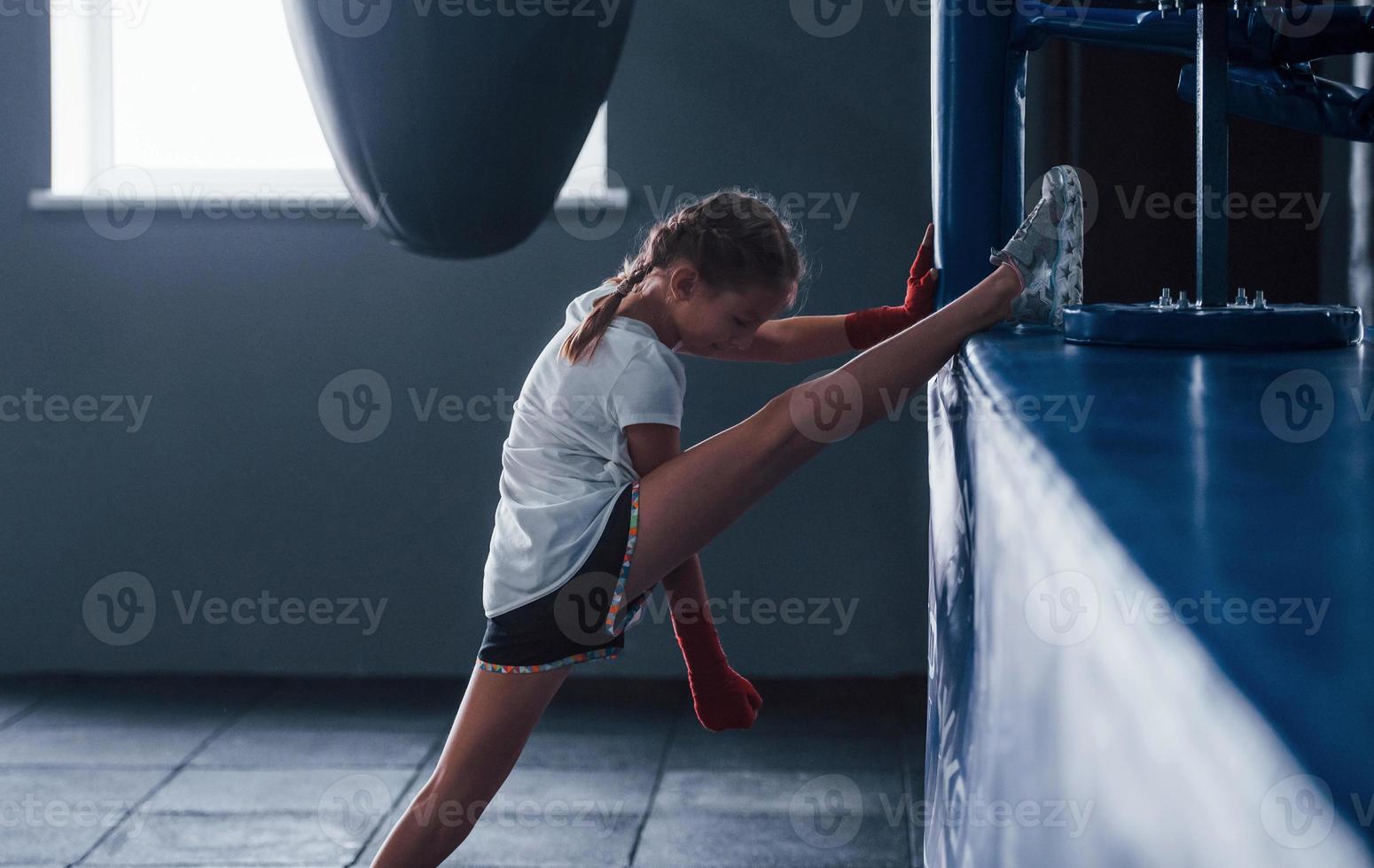 estiramiento antes de los ejercicios. una niña pequeña con ropa deportiva está en el gimnasio y tiene un día de ejercicio. concepción del boxeo foto