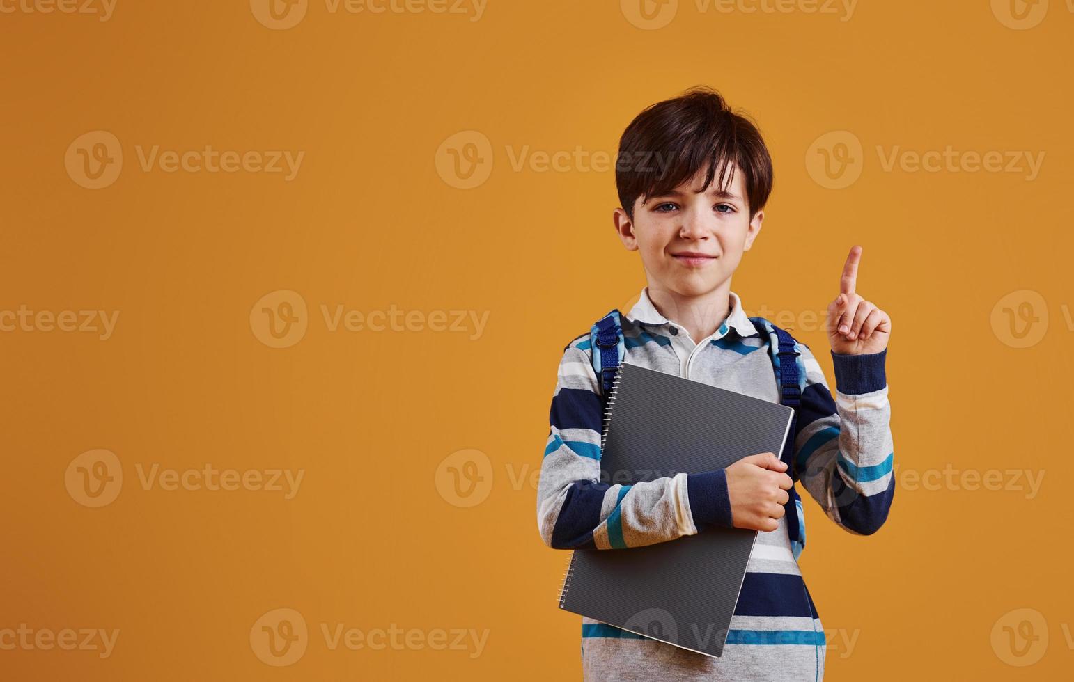 Portrait of young smart schooler in the studio against yellow background photo