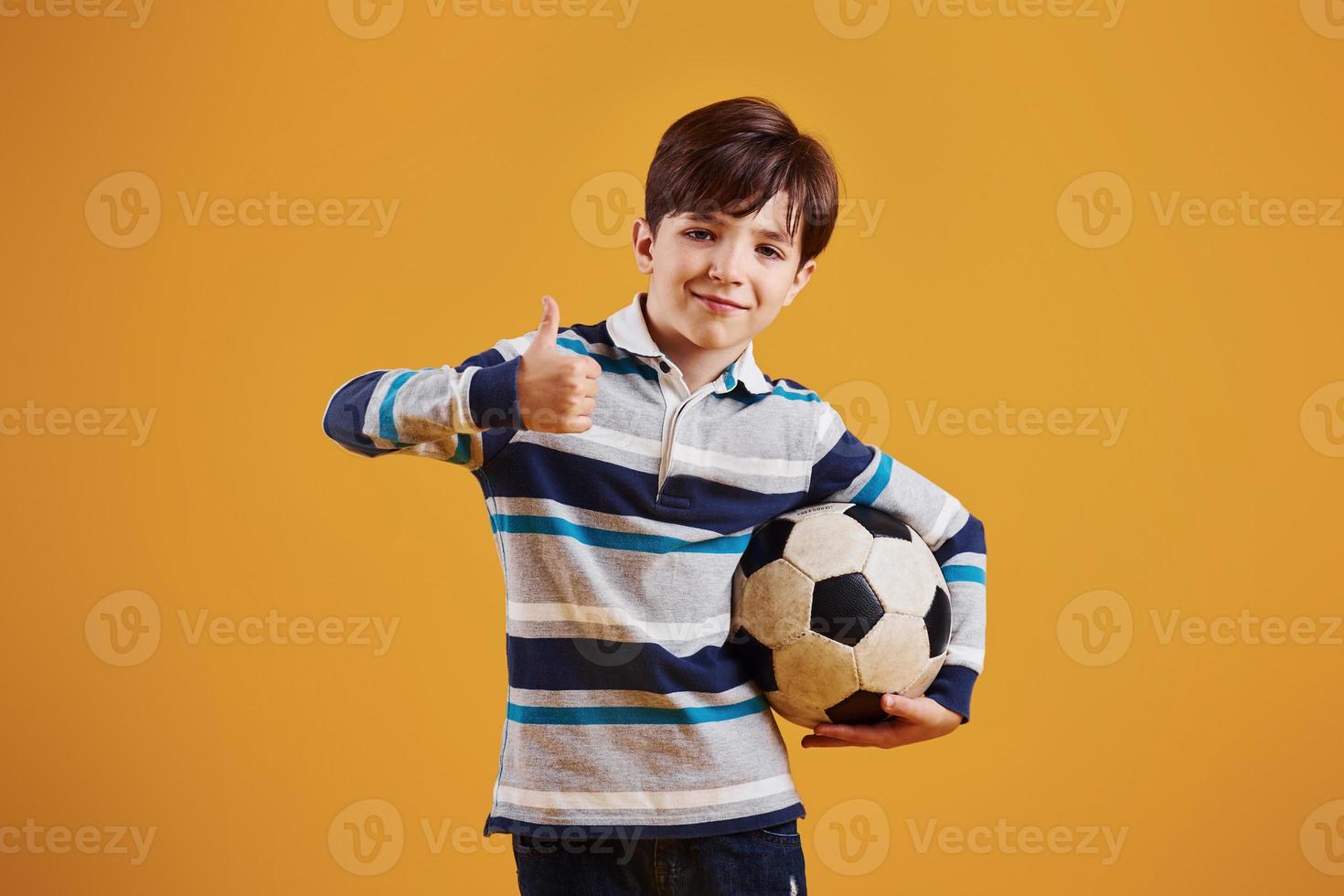 Portrait of young soccer player with ball. Stands against yellow background photo