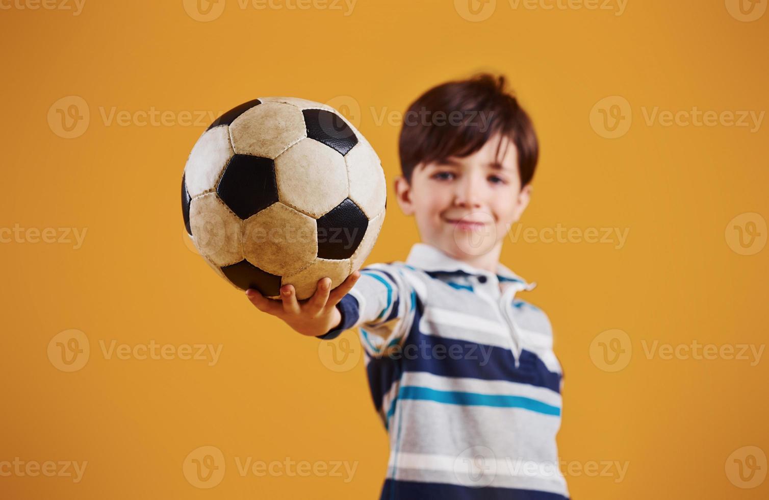 retrato de joven futbolista con balón. se encuentra contra el fondo amarillo foto