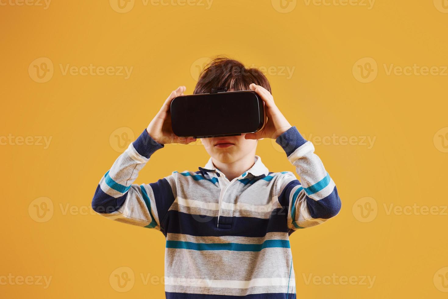 lindo niño pequeño con gafas de realidad virtual en el estudio con fondo amarillo foto