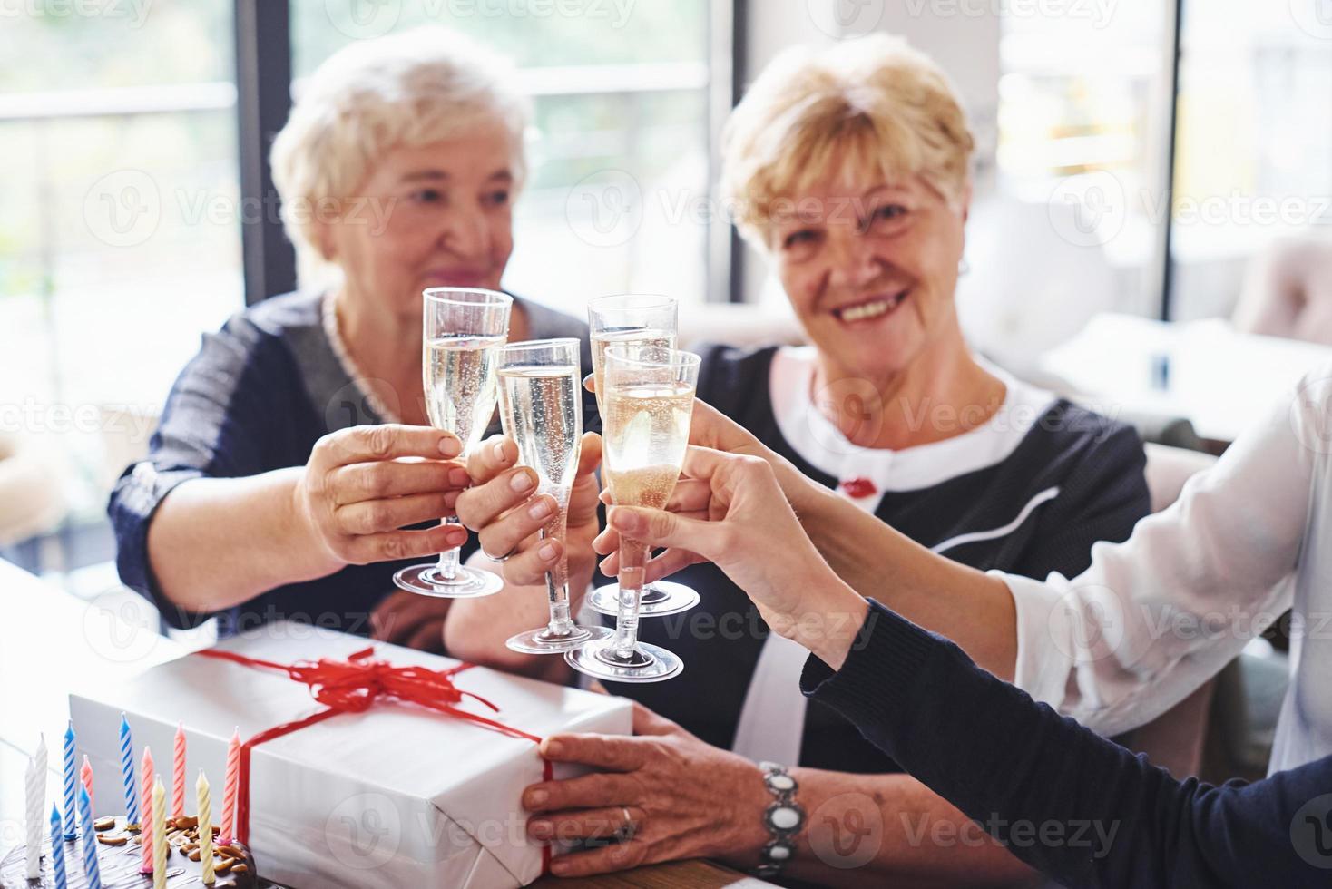 Knocking glasses. Senior woman with family and friends celebrating a birthday indoors photo