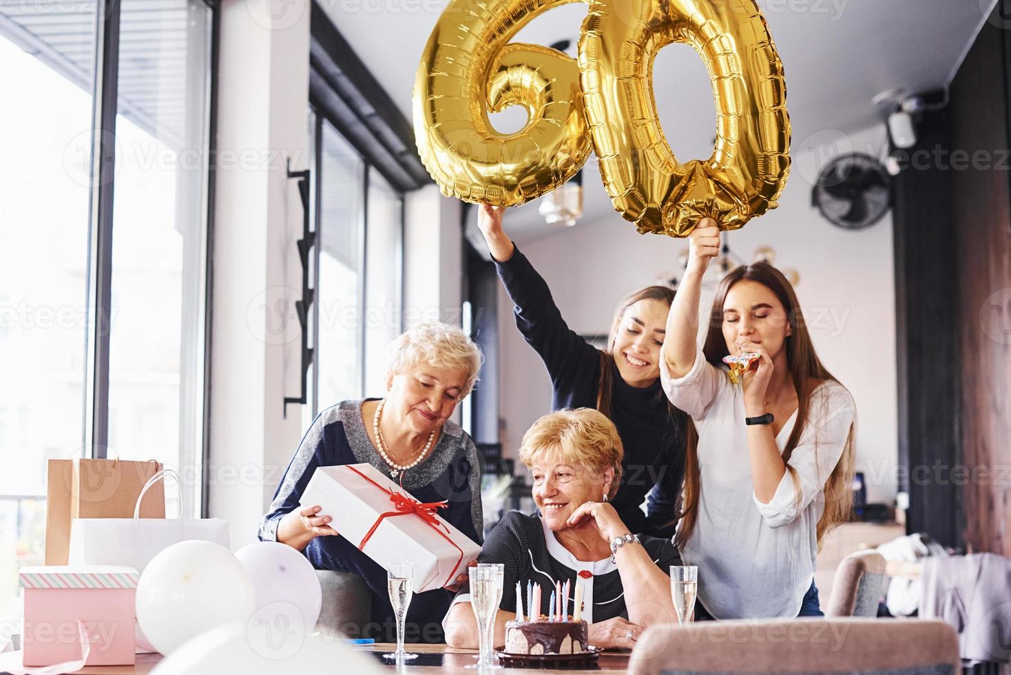 globos con el número 60. mujer mayor con familiares y amigos celebrando un cumpleaños en el interior foto