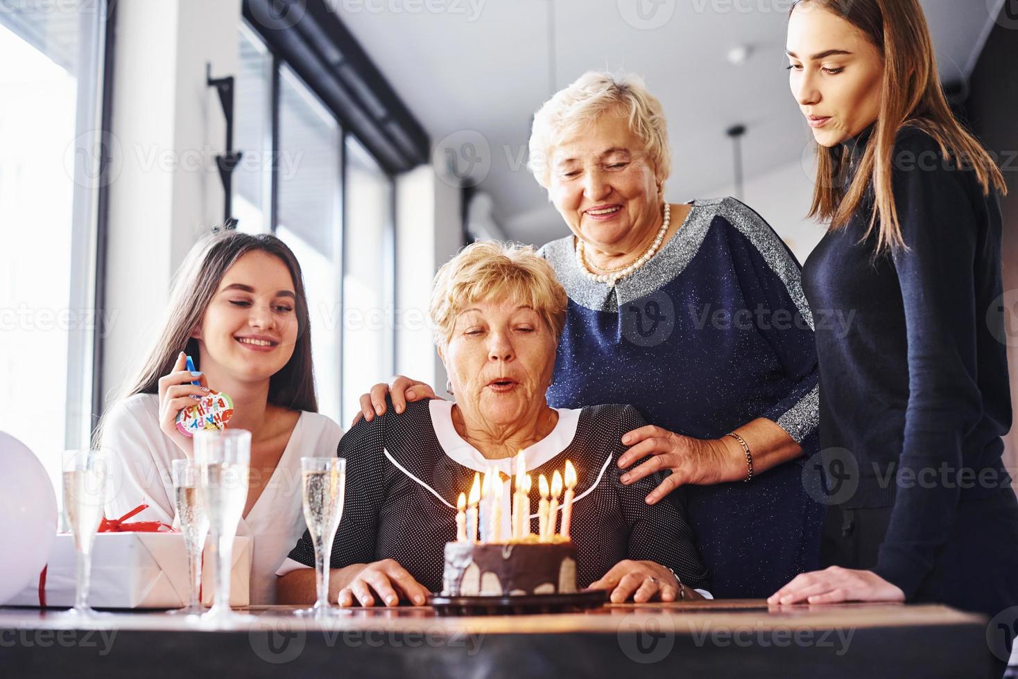 Blowing the candles. Senior woman with family and friends celebrating a birthday indoors photo