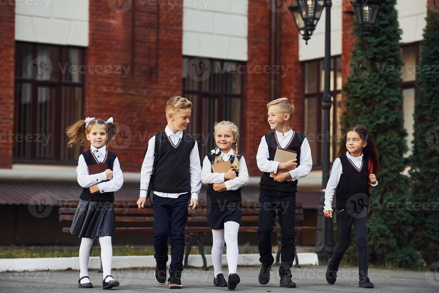 grupo de niños con uniforme escolar que están juntos al aire libre cerca del edificio de educación foto