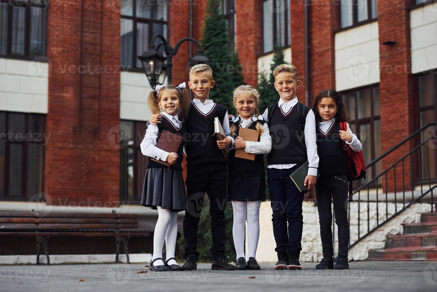 grupo de niños con uniforme escolar que están juntos al aire libre cerca del edificio de educación foto