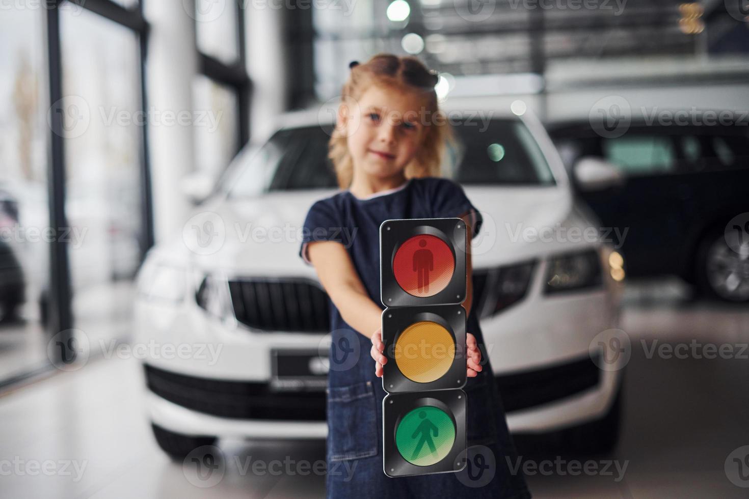 Portrait of cute little girl that holds traffic lights picture in hands in automobile salon photo