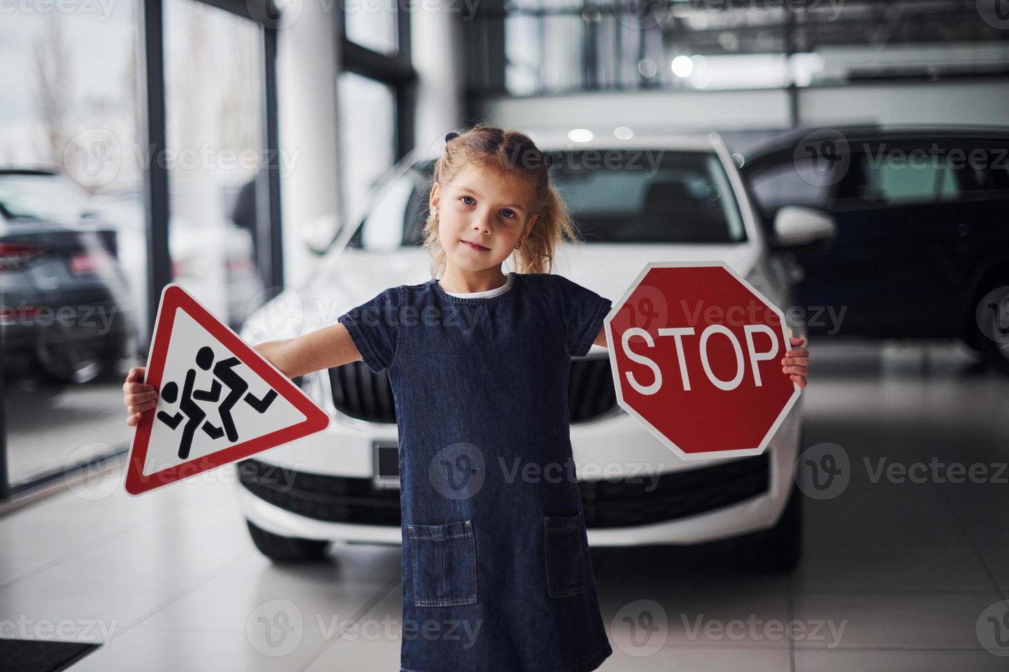 Portrait of cute little girl that holds road signs in hands in automobile salon photo