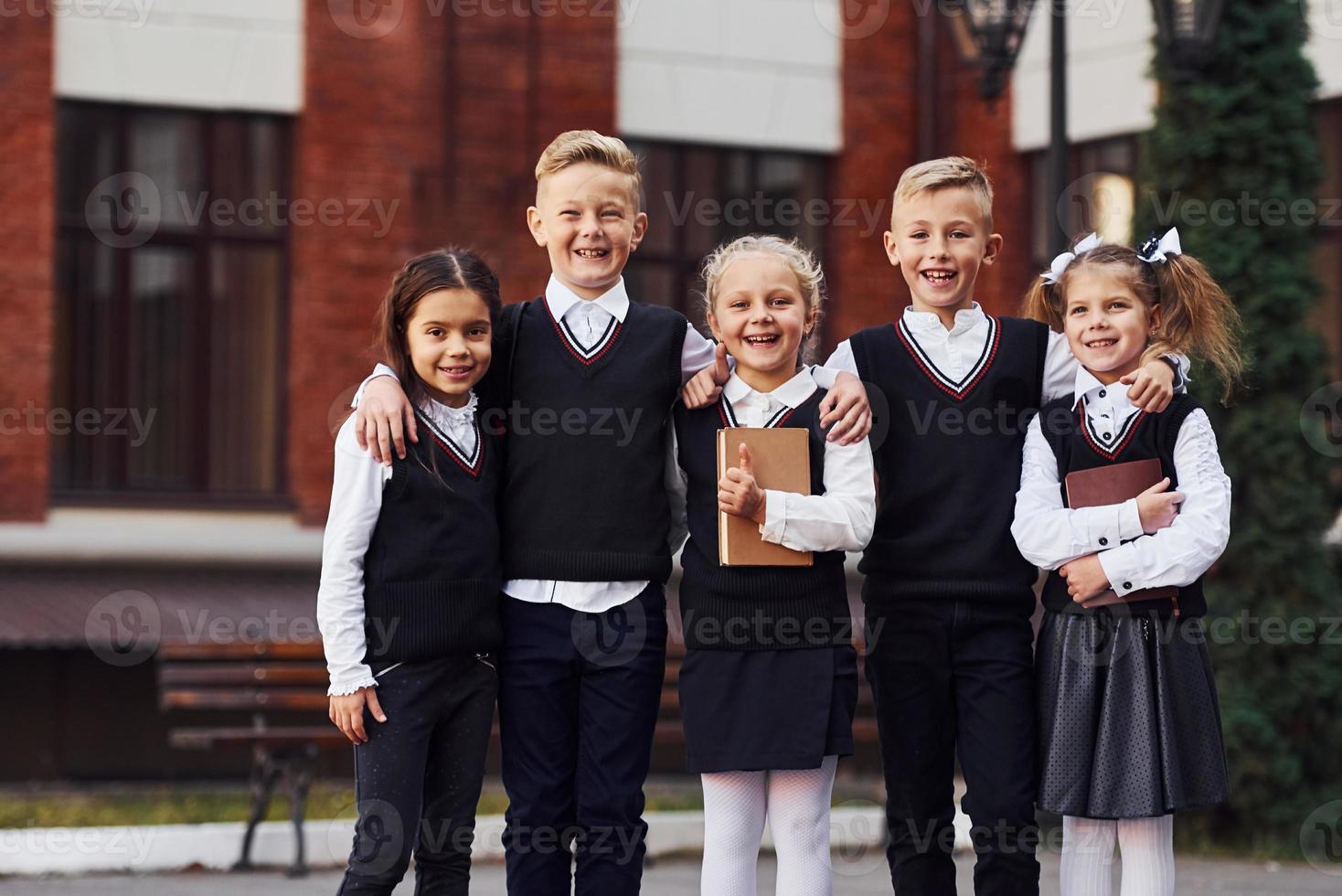 grupo de niños con uniforme escolar que están juntos al aire libre cerca del edificio de educación foto