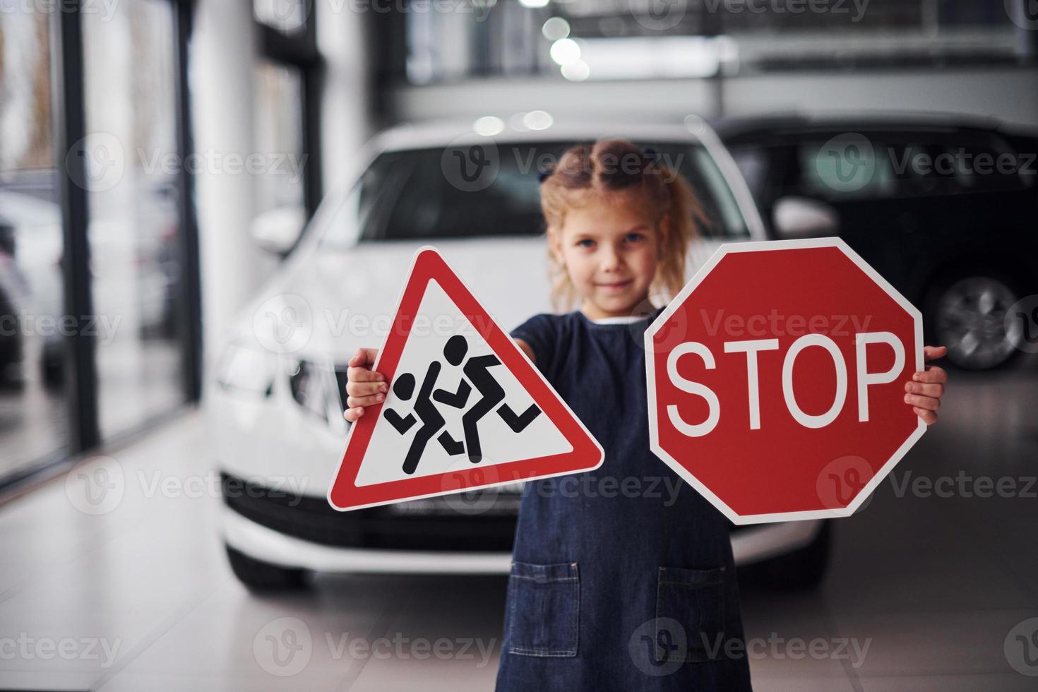 Portrait of cute little girl that holds road signs in hands in automobile salon photo