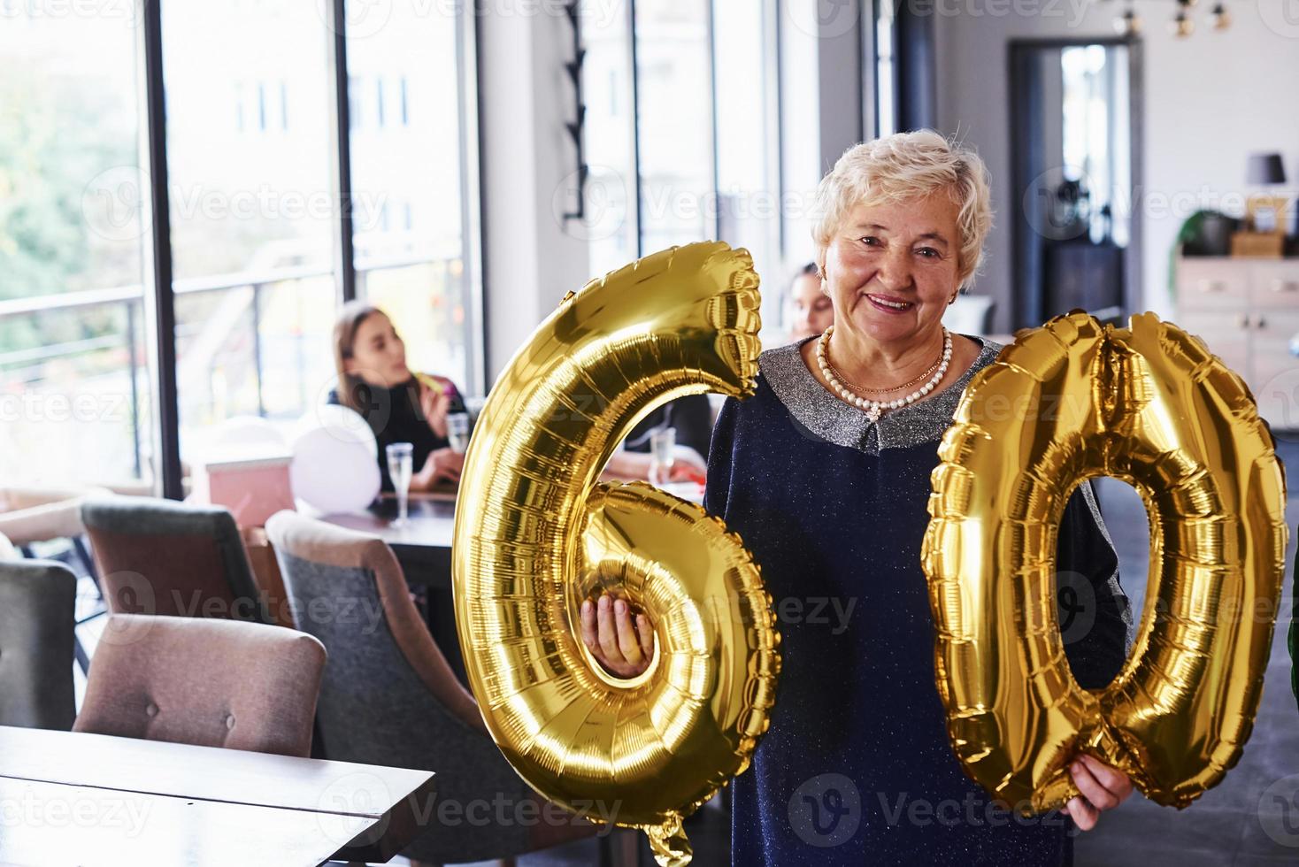 con globos del número 60 en las manos. mujer mayor con familiares y amigos celebrando un cumpleaños en el interior foto