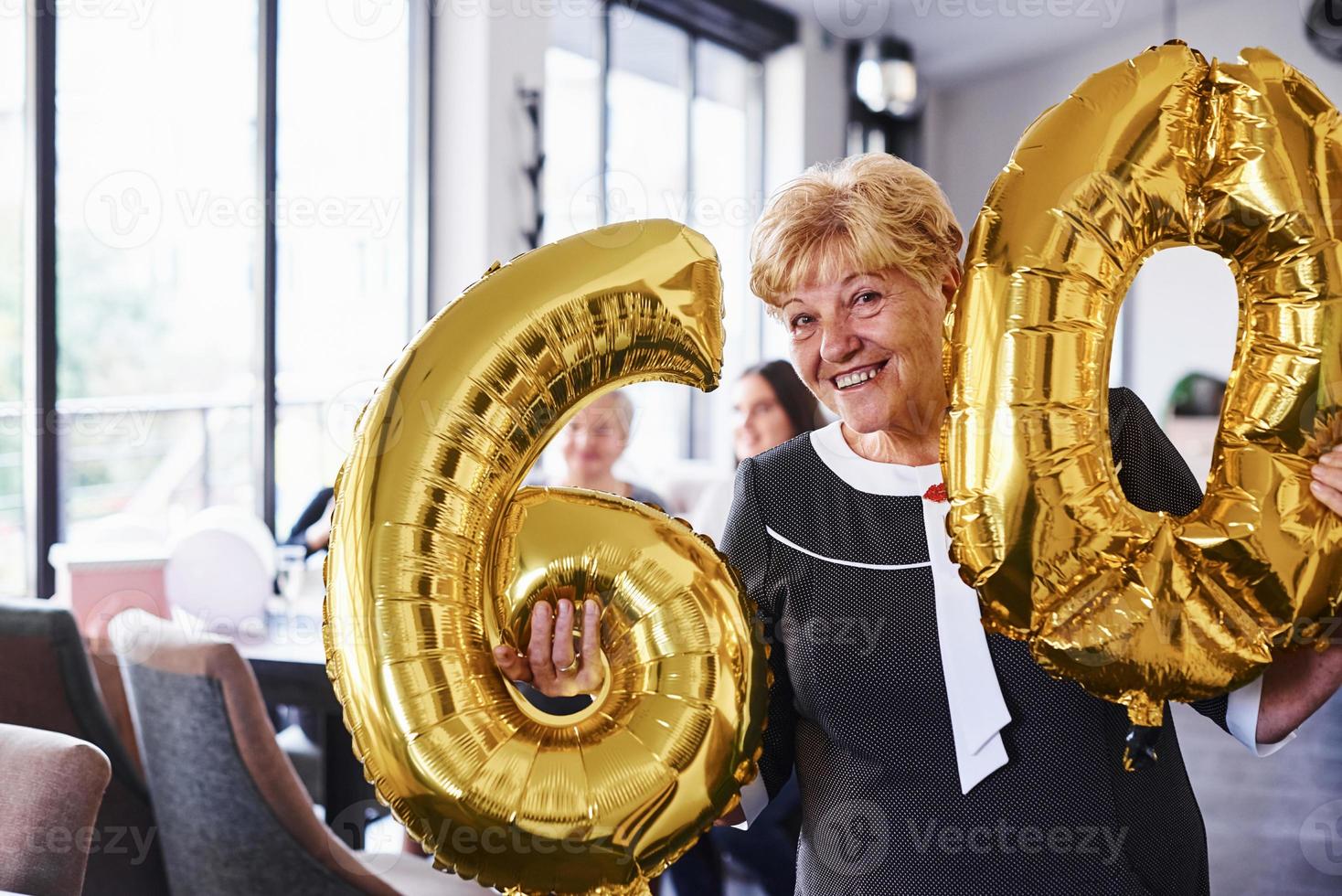 con globos del número 60 en las manos. mujer mayor con familiares y amigos celebrando un cumpleaños en el interior foto