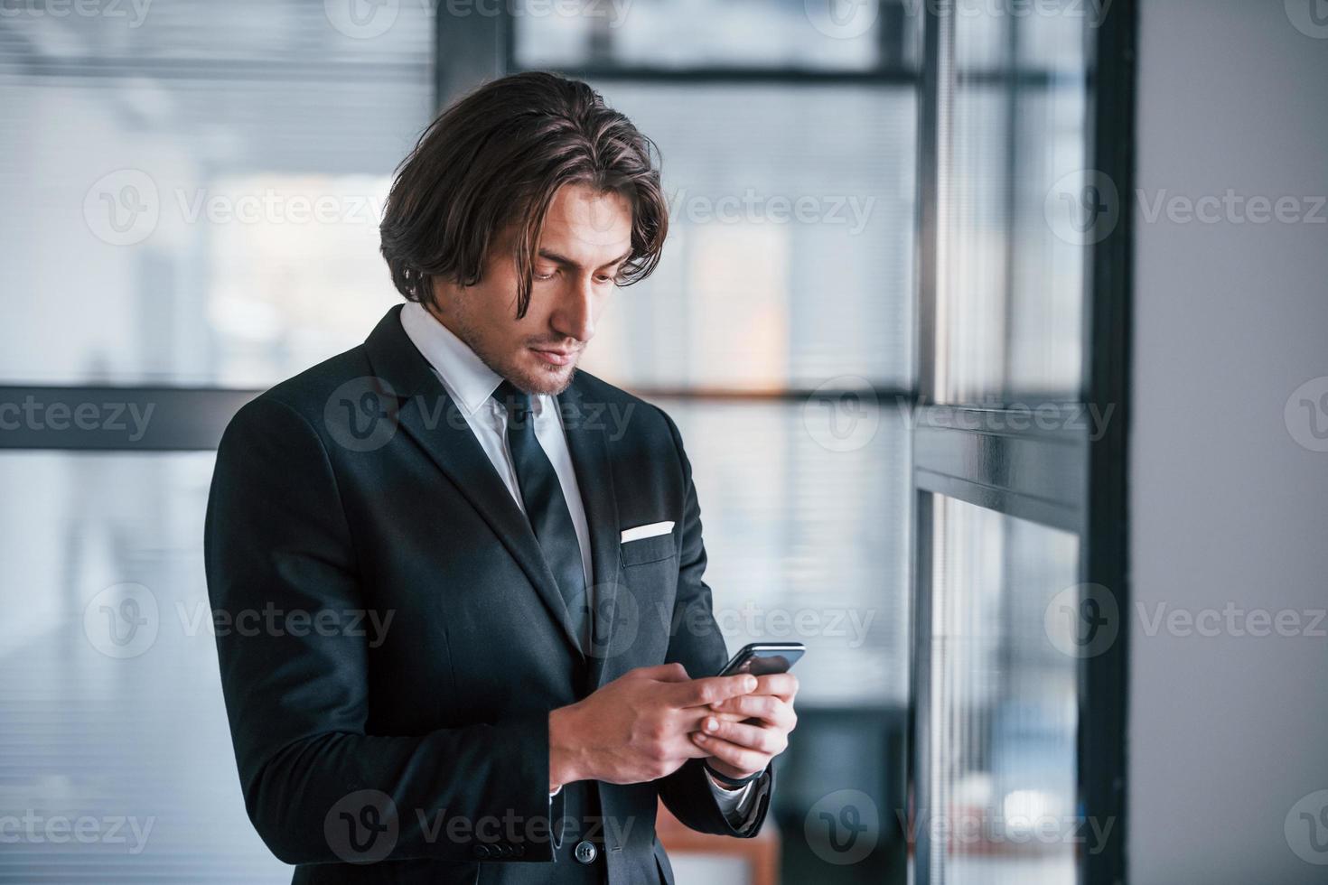 usando el teléfono retrato de un apuesto joven hombre de negocios con traje negro y corbata foto