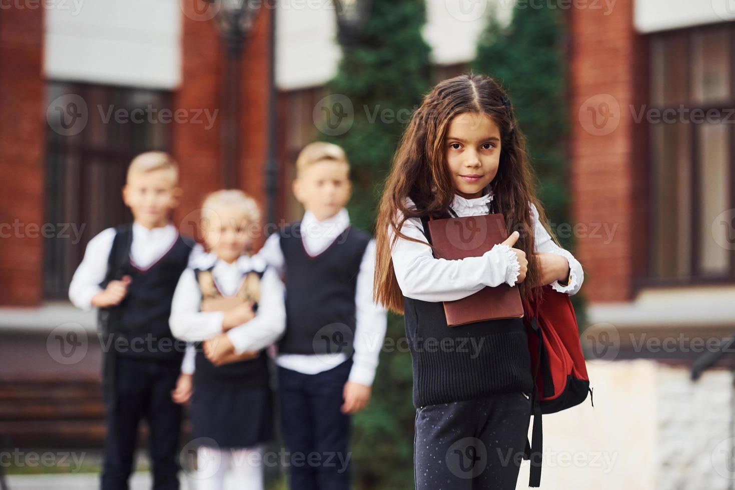 Group of kids in school uniform posing to the camera outdoors together near education building photo