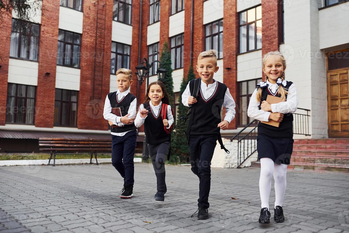 Group of kids in school uniform posing to the camera outdoors together near education building photo