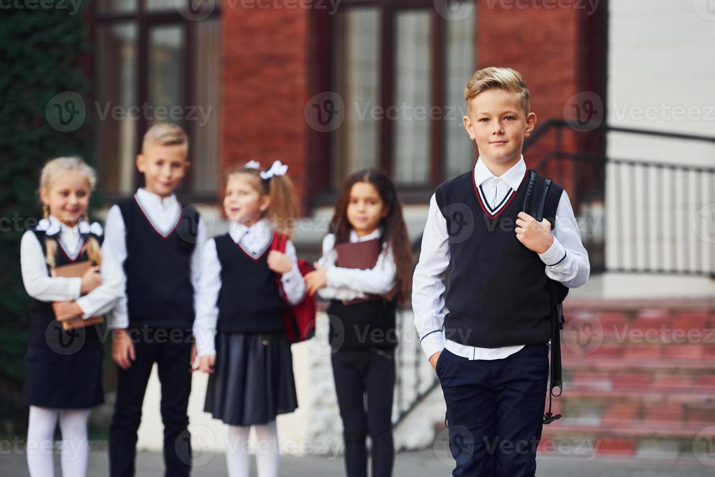 Group of kids in school uniform posing to the camera outdoors together near education building photo