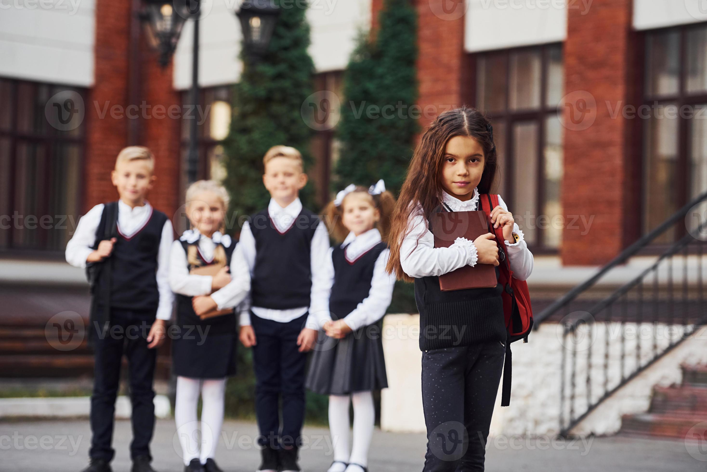Group of kids in school uniform posing to the camera outdoors together near education building