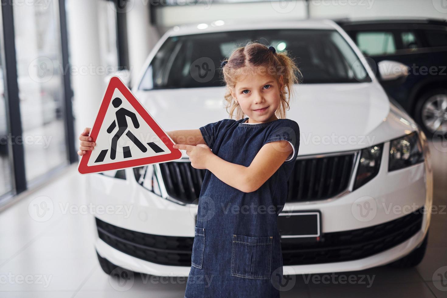 Portrait of cute little girl that holds road sign in hands in automobile salon photo