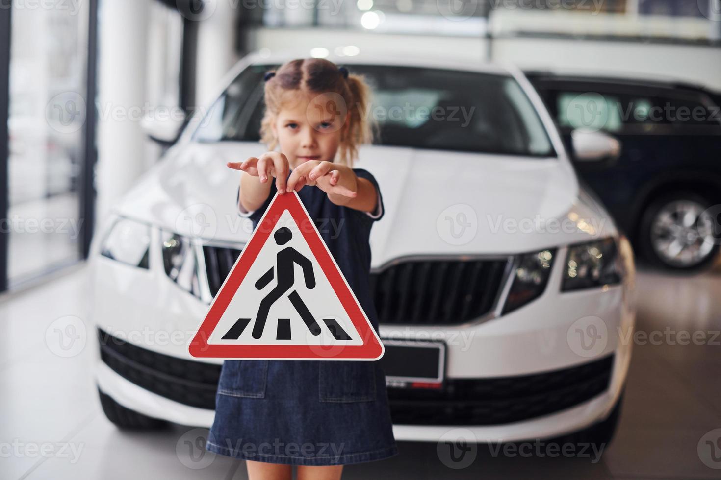 Portrait of cute little girl that holds road sign in hands in automobile salon photo