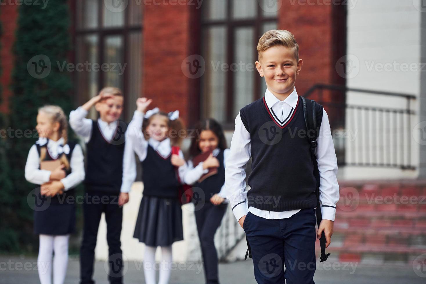 Group of kids in school uniform posing to the camera outdoors together near education building photo