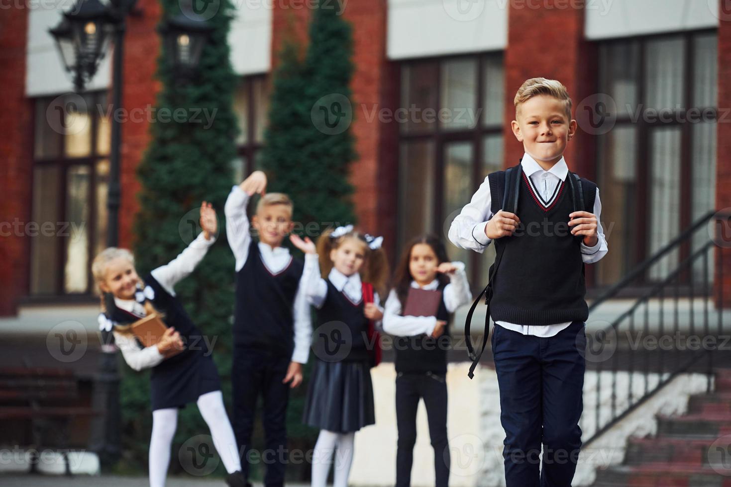 Group of kids in school uniform posing to the camera outdoors together near education building photo