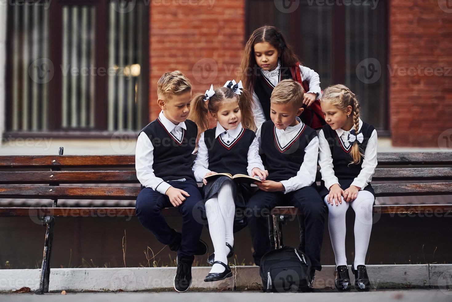 niños de la escuela en uniforme que se sienta al aire libre en el banco con bloc de notas foto