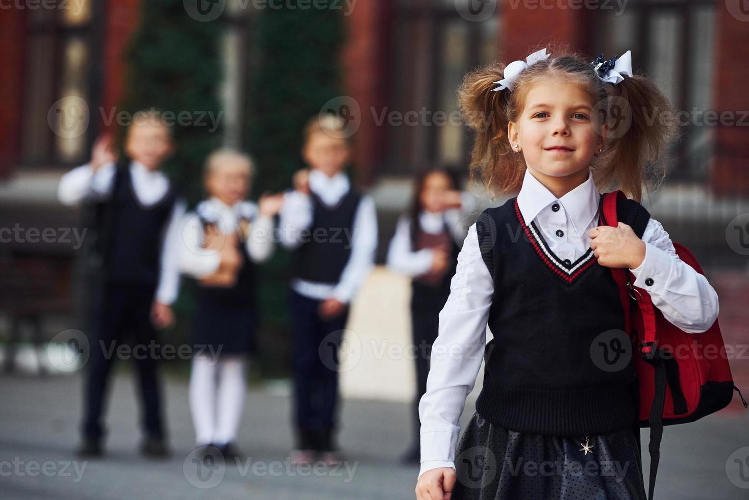 Group of kids in school uniform posing to the camera outdoors together near education building photo