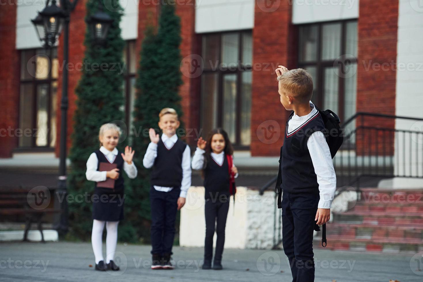 Group of kids in school uniform posing to the camera outdoors together near education building photo