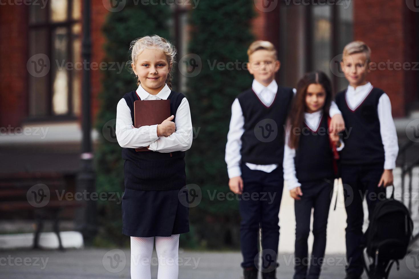Group of kids in school uniform posing to the camera outdoors together near education building photo