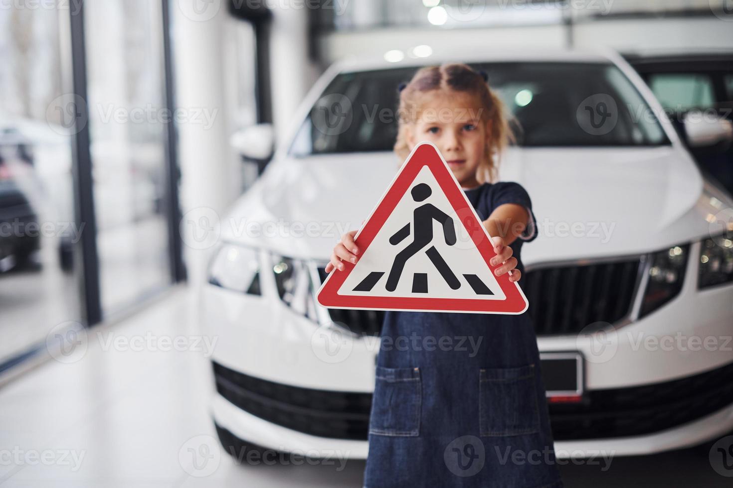 Portrait of cute little girl that holds road sign in hands in automobile salon photo