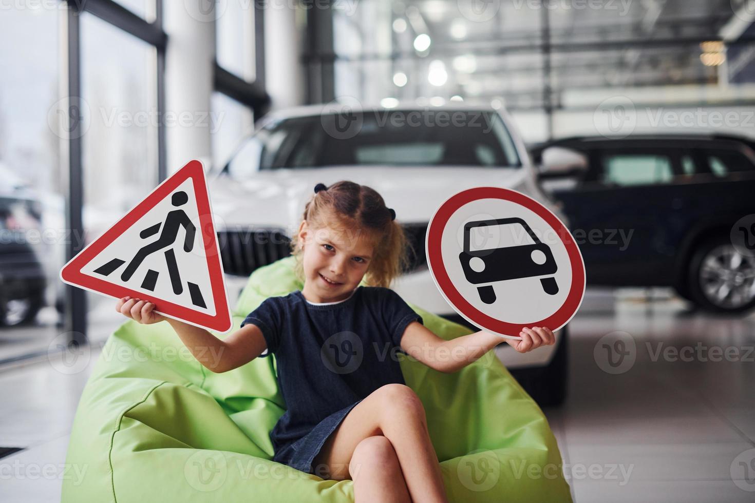 Portrait of cute little girl that holds road signs in hands in automobile salon photo