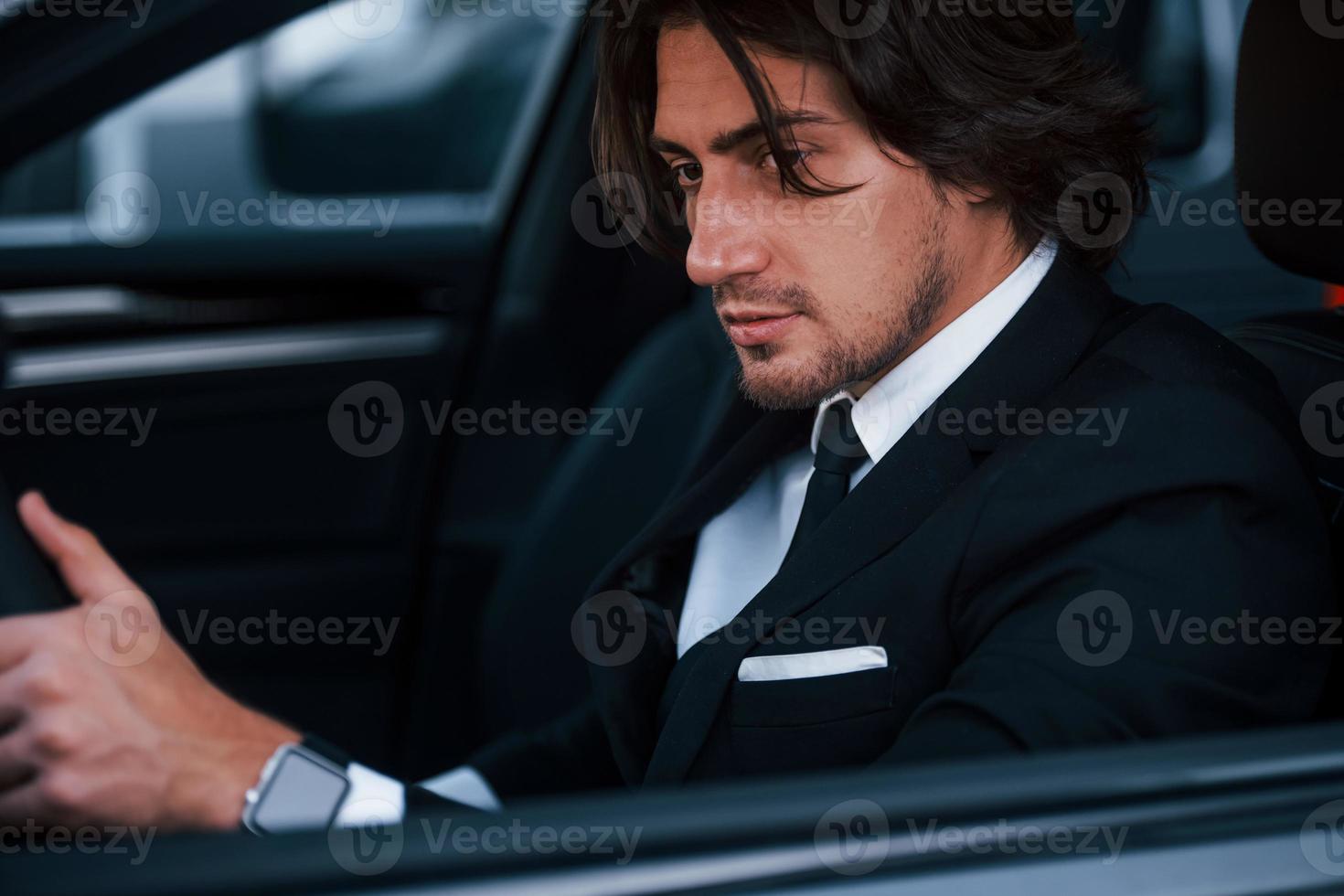Young businessman in black suit and tie inside modern automobile photo