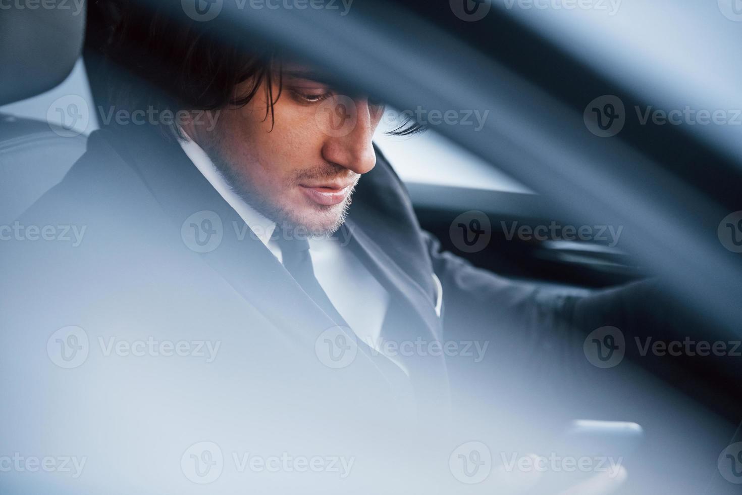 Young businessman in black suit and tie inside modern automobile photo