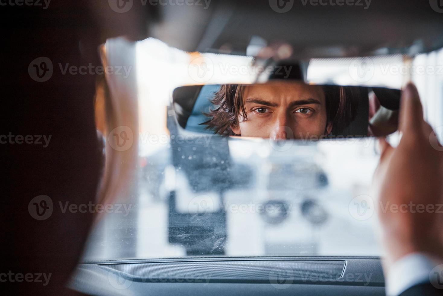 joven hombre de negocios con traje negro y corbata conduciendo un automóvil moderno foto