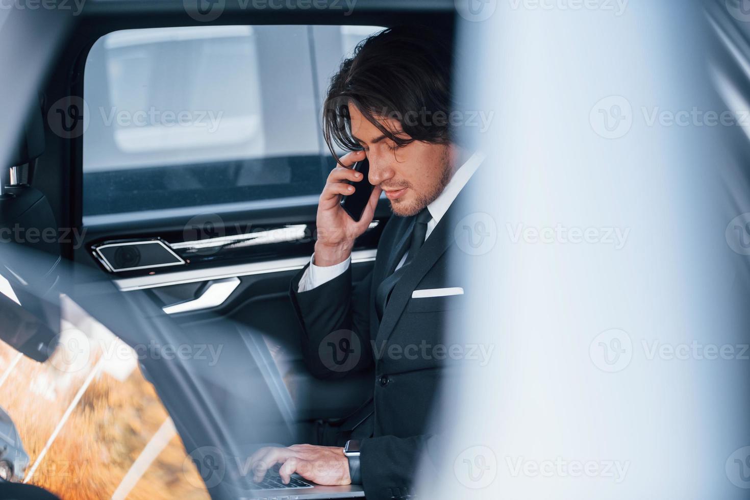 Young businessman in black suit and tie inside modern automobile photo