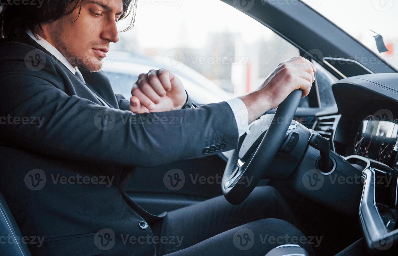 joven hombre de negocios con traje negro y corbata conduciendo un automóvil moderno foto