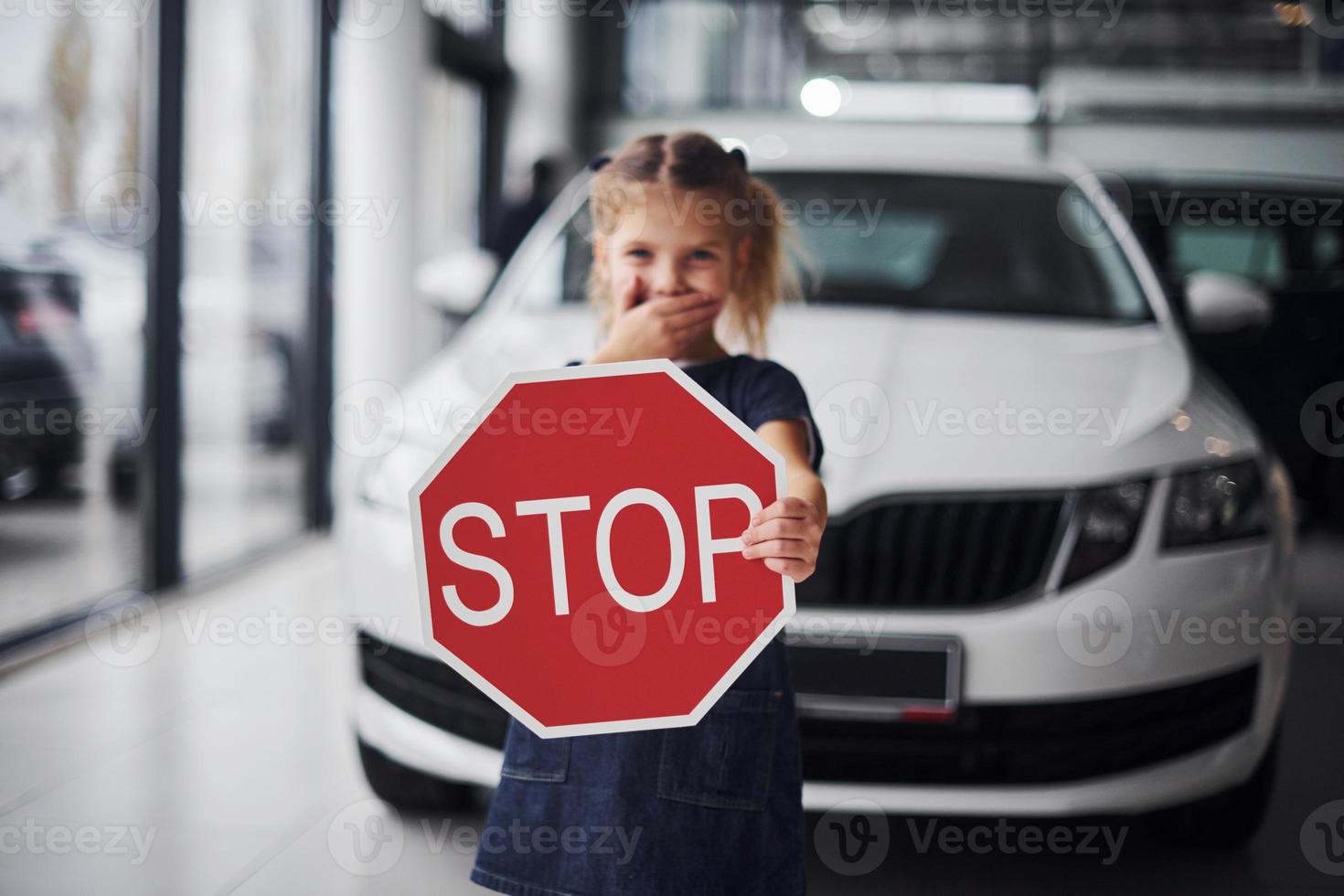 Portrait of cute little girl that holds road sign in hands in automobile salon photo