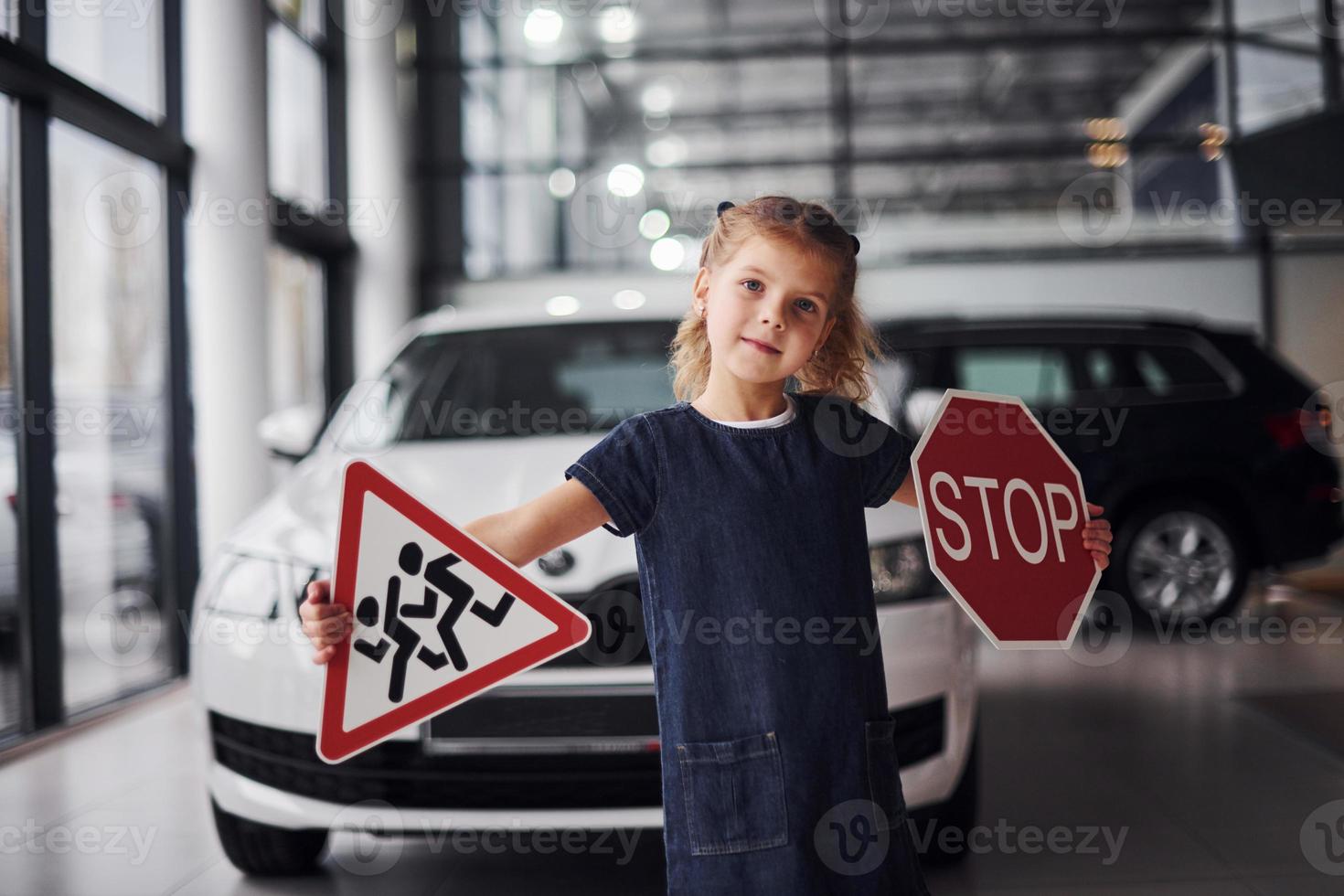 Portrait of cute little girl that holds road signs in hands in automobile salon photo