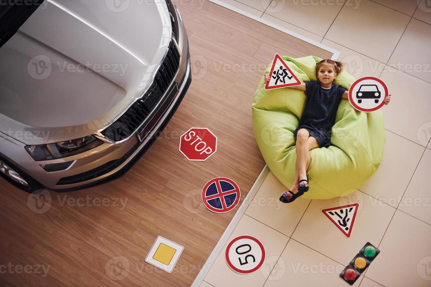Top view of cute little girl that holds road signs in hands in automobile salon photo